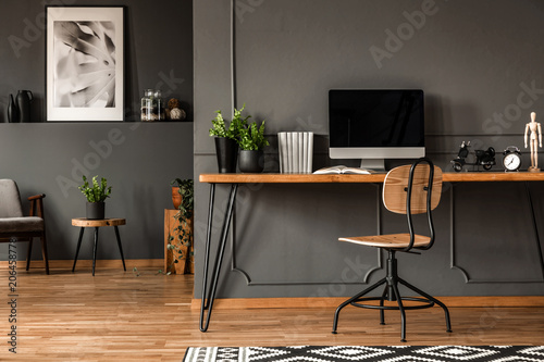 Real photo of an open space interior with black walls and molding. Workspace with desk, chair and computer in the foreground and living room with gray armchair at the back
