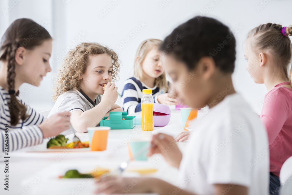 Group of children eating vegetables in the dining hall of school Group of children eating vegetables in the dining hall of school