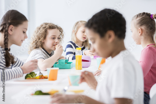 Group of children eating vegetables in the dining hall of school