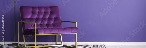 Purple armchair with gold metal frame standing on patterned black and white carpet in violet reading room interior. Place your product here