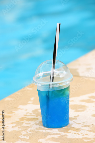 blue summer cocktail in plastic glass with straw near the pool on background of bright turquoise water