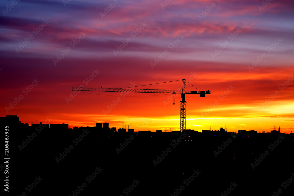 Industrial construction cranes and building silhouettes at sunset Industrial construction cranes and building silhouettes at sunset