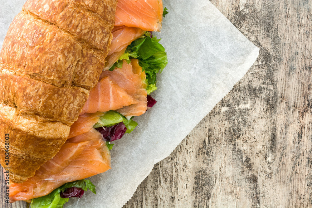 Croissant sandwich with salmon and vegetables on wooden table. Copyspace
