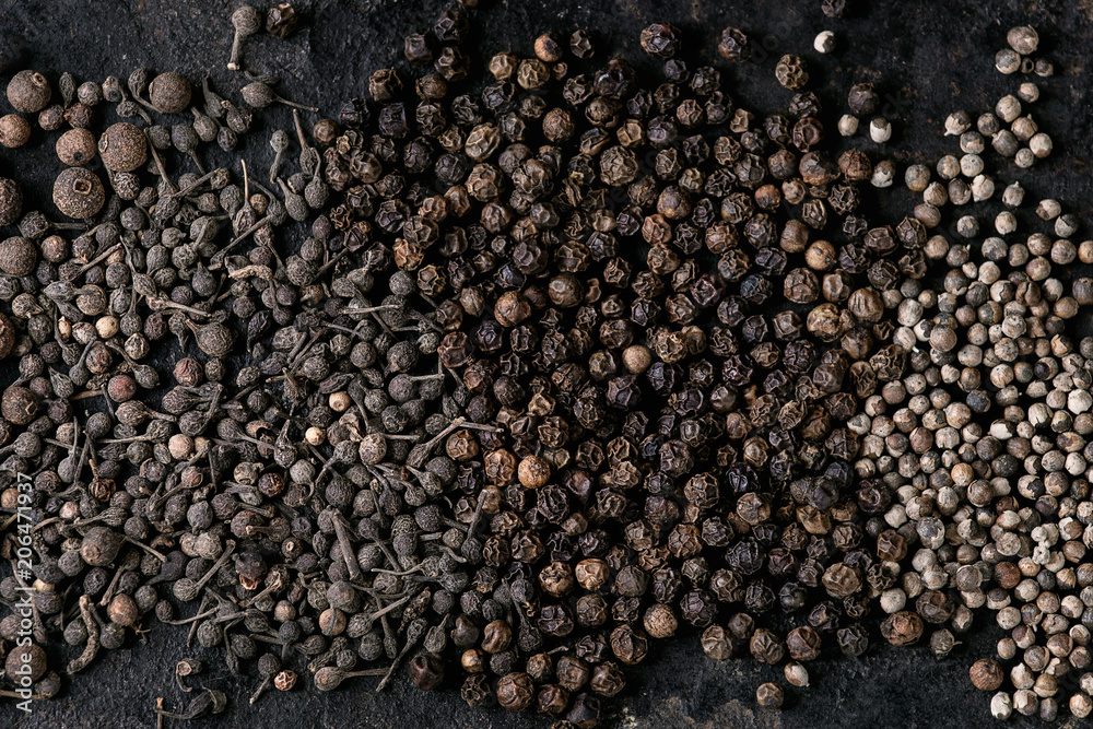 Variety of different black peppers allspice, pimento, monks pepper, peppercorns over old black iron texture surface. Food background. Top view, space. Variety of different black peppers allspice, pimento, monks pepper, peppercorns over old black iron texture surface. Food background. Top view, space.