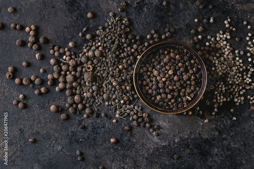 Tela Variety of different black peppers allspice, pimento, monks pepper, peppercorns and ground powder in tin can over old black iron texture background