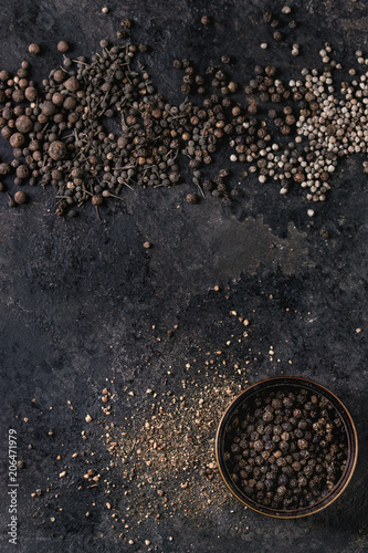 Variety of different black peppers allspice, pimento, monks pepper, peppercorns and ground powder in tin can over old black iron texture surface. Top view, space. Food background