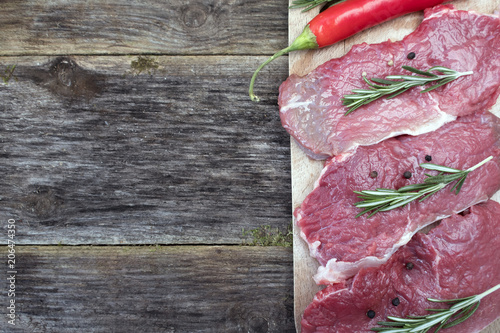 Raw pork steak with black pepper peas and rosemary close-up on a wooden background and copy space