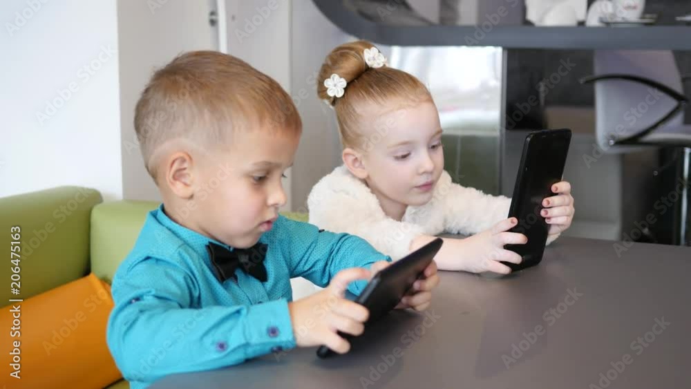 Cute kids boy and girl watch use tablet computer display sitting at cafe table Cute kids boy and girl watch use tablet computer display sitting at cafe table