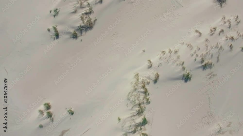 Flying over sand dunes. Shooting from helicopter. Texture of sand dunes white color. White sandy surface with hills and green bushes and grass. View from above of desert barkhans Flying over sand dunes. Shooting from helicopter. Texture of sand dunes white color. White sandy surface with hills and green bushes and grass. View from above of desert barkhans