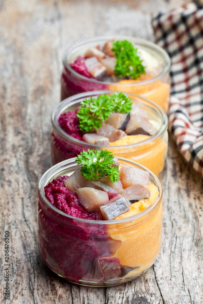 Herring salad with colorful vegetables in a small glass jars on wooden table Herring salad with colorful vegetables in a small glass jars on wooden table