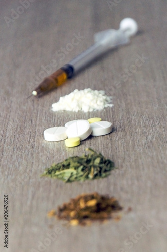 the road to death: in a row are narcotic substances in the degree of increased exposure and danger, tobacco, weed, amphetamine, cocaine and heroin, front top, short focus on tablets
