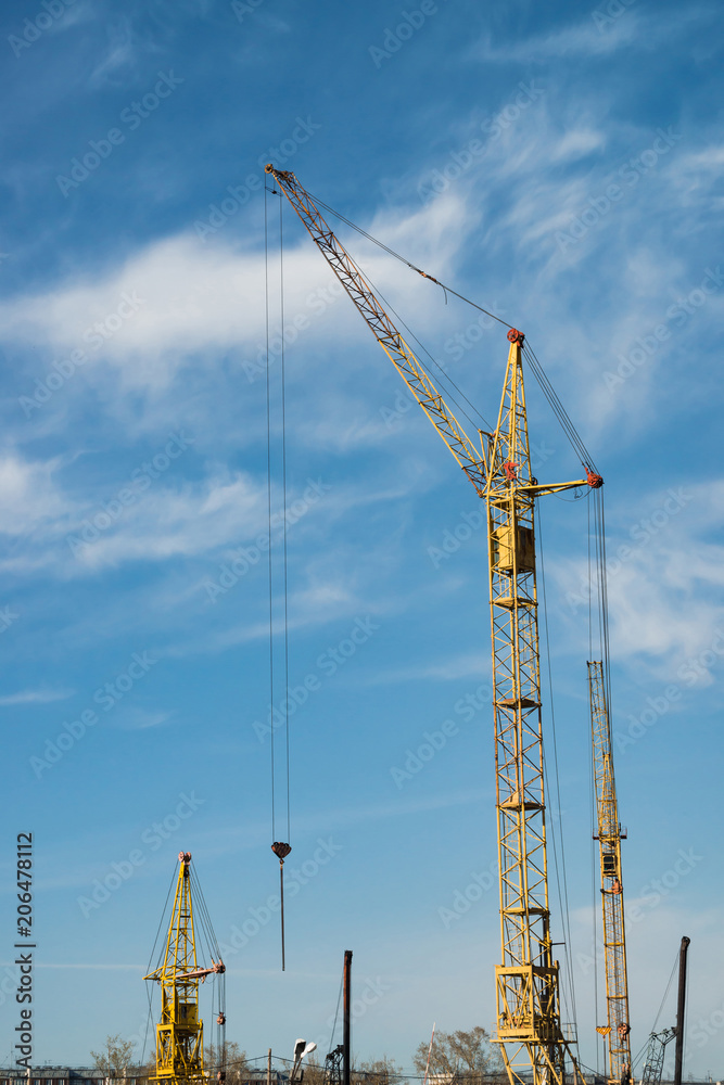 Big tower cranes against the blue sky. Background image of construction equipment close-up with copy space. Build of city.