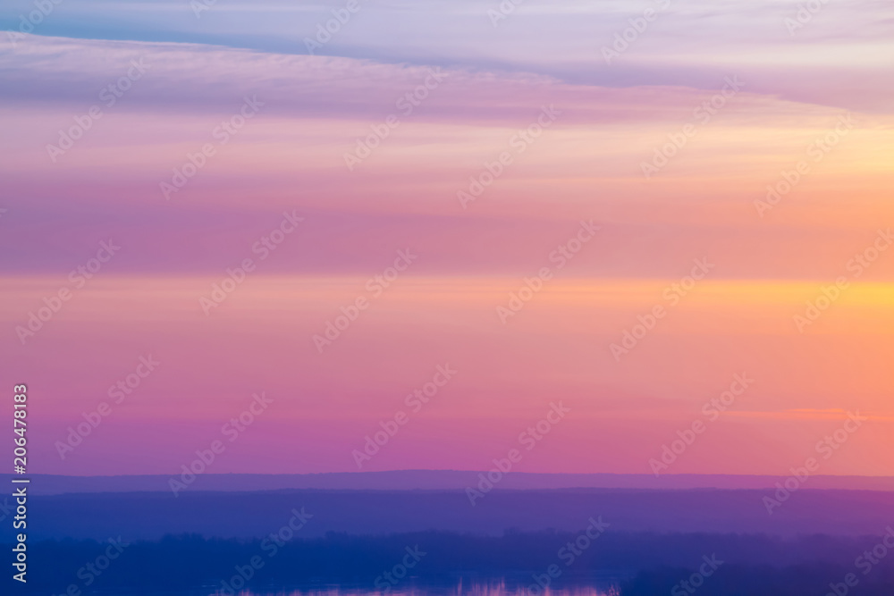 Varicolored striped surreal sky with shades of blue, cyan, pink, purple, magenta colors with cobalt land and lake. Horizontal lines of smooth clouds. Atmospheric image of tender sky, land and river.