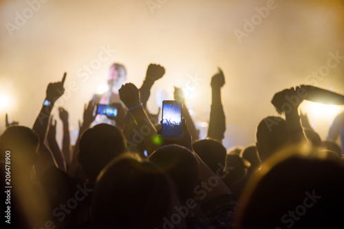 Silhouettes of people in a bright in the pop rock concert in front of the stage. Hands with gesture Horns. That rocks. Party in a club