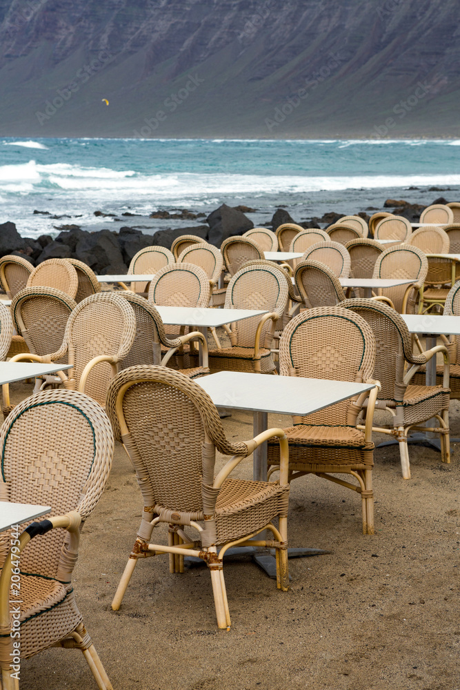 LANZAROTE, CANARY ISLANDS, SPAIN: Low season - empty tables and chairs on the terraces of Famara, with the sea and cliffs in the background.