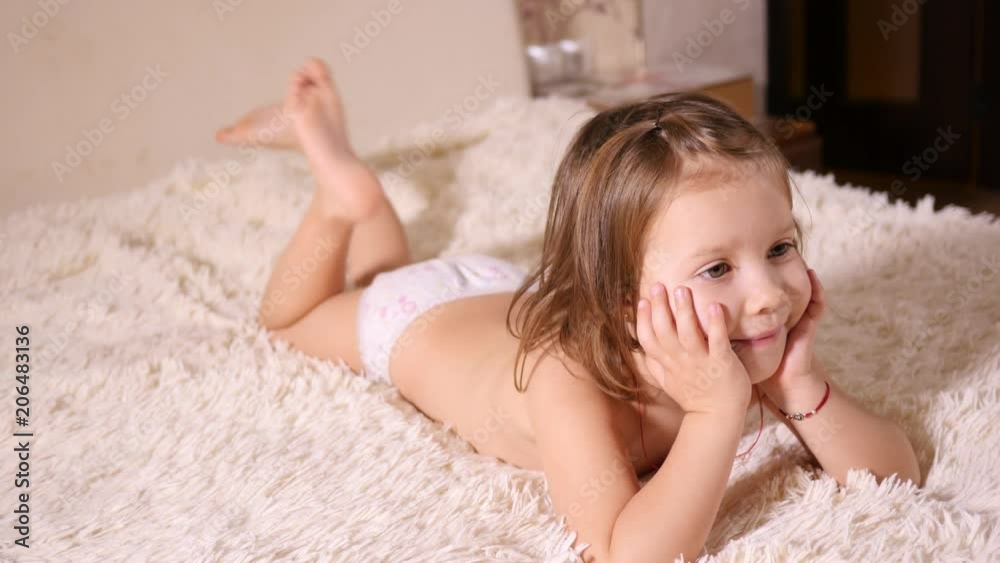 Little funny child girl lying on a bed watching TV does not want go to sleep