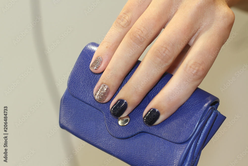 Beautiful female hand with manicure holds blue leather wallet. Dark blue and brilliant silver nail polish.