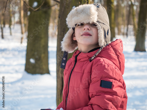 Cute little boy in red jacket at winter park background