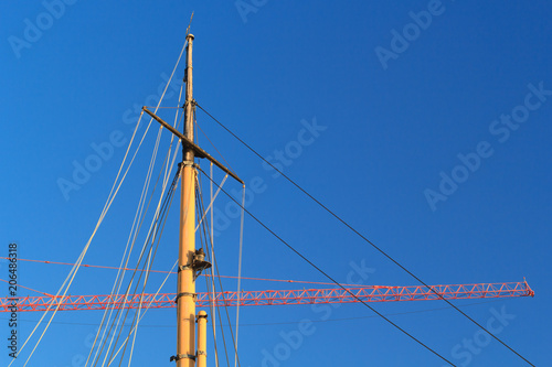 Ships mast with construction crane arm or jib in background.