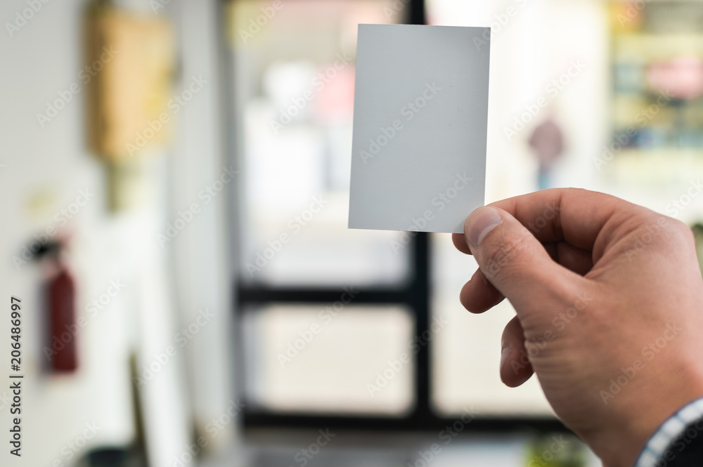 Closeup image of holding business card, person hand showing plain mock up space on professional office background. Businessman communication information Closeup image of holding business card, person hand showing plain mock up space on professional office background. Businessman communication information