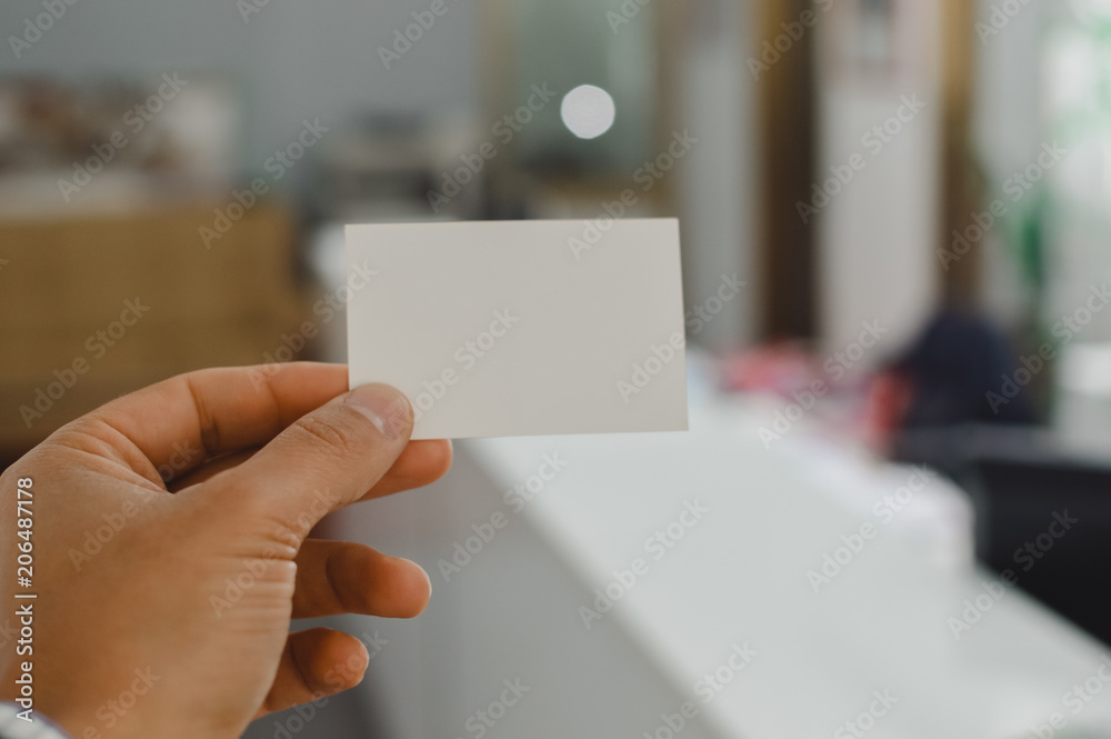 Closeup image of holding business card, person hand showing plain mock up space on professional office background. Businessman communication information Closeup image of holding business card, person hand showing plain mock up space on professional office background. Businessman communication information