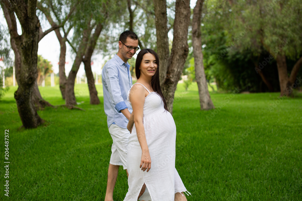 Pregnant couple walks in the park together holding hands Pregnant couple walks in the park together holding hands