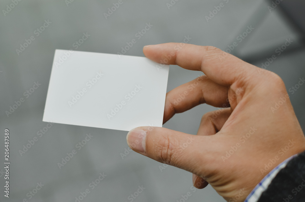 Closeup image of holding business card, person hand showing plain mock up space on professional office background. Businessman communication information Closeup image of holding business card, person hand showing plain mock up space on professional office background. Businessman communication information