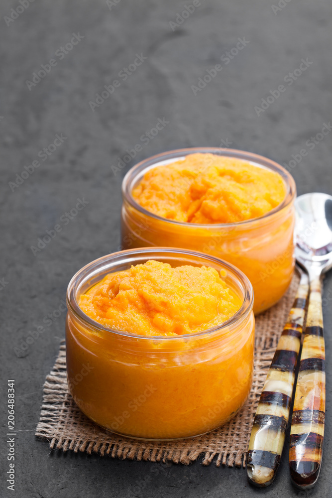 Orange vegetables puree in glass jars on black stone background Orange vegetables puree in glass jars on black stone background