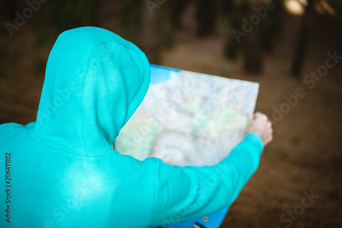 Rear view of traveler in blue hoodie checking the map while resting in pine forest photo