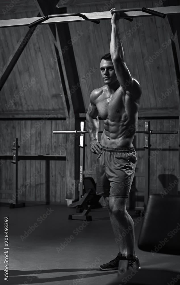Strong athletic man going to do pulling up on horizontal bar, black and white image