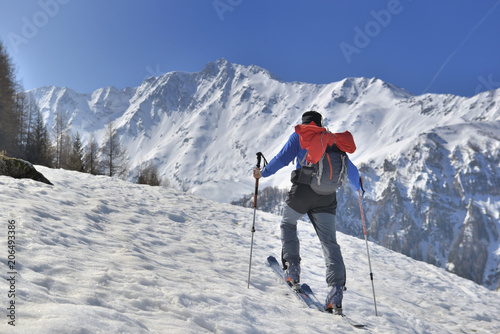 man climbing snowy mountain in touring ski under blue sky 
