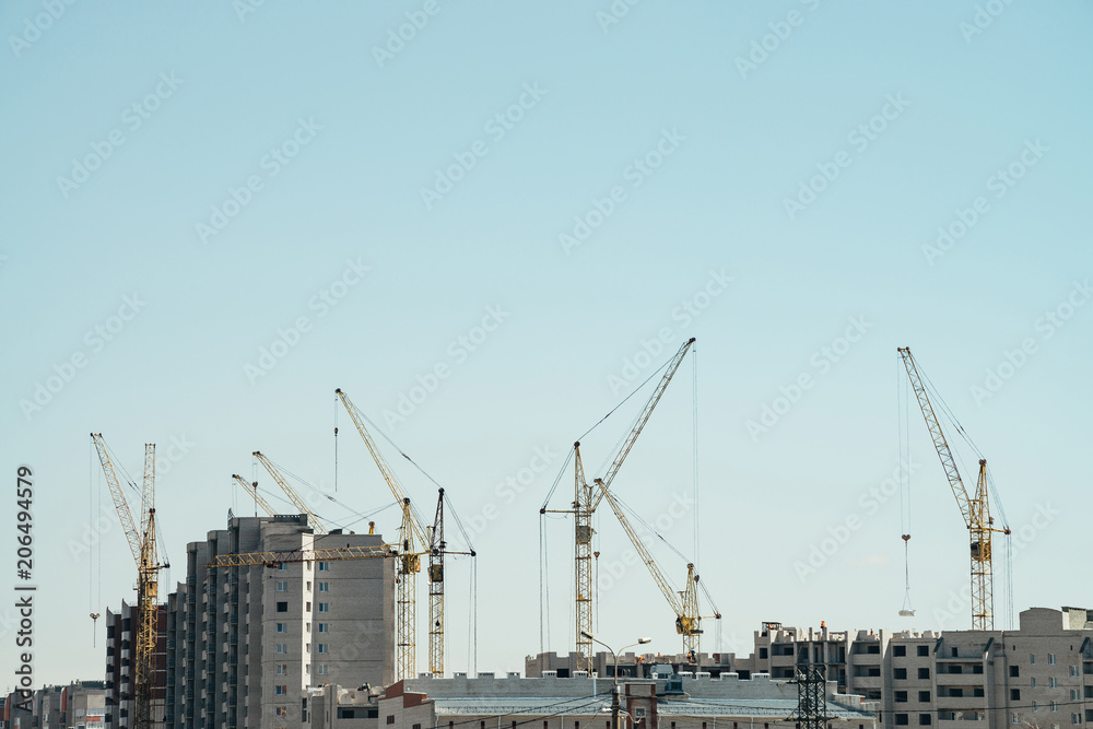 View of construction of close-up. Group of multifamily building in process of construction. Many cranes in work. Little builders on roofs of buildings. Cityscape with cranes, buildings and workers.