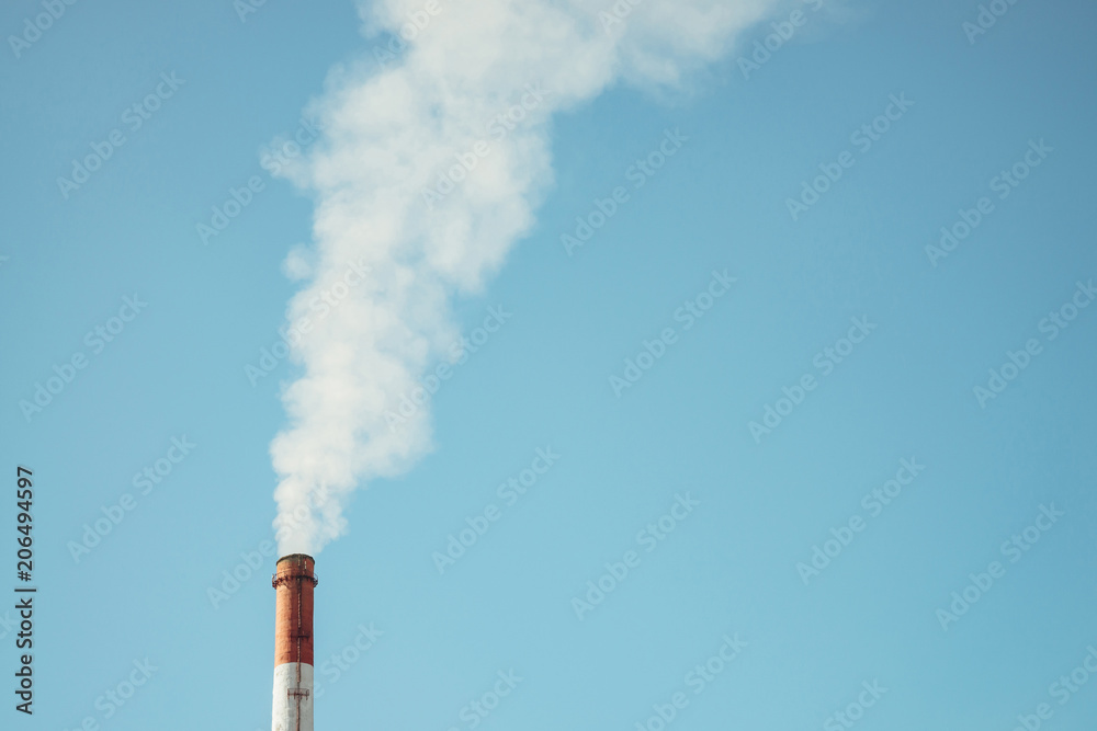 High red and white tower of CHPP close-up. White steam from striped pipe of CHP on blue sky. Industrial background image of TPP with copy space. Thermal power plant produce steam for electric power.