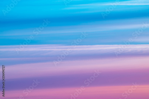 Varicolored striped surreal sky with shades of blue, cyan, cobalt, pink, purple, magenta colors. Horizontal lines of smooth clouds. Atmospheric background image of tender sky.