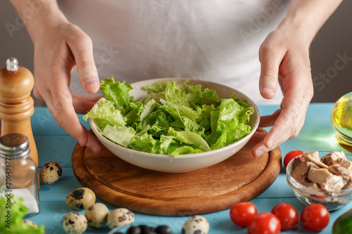 Hands take bowl with lettuce salad leaves from kitchen table with food.