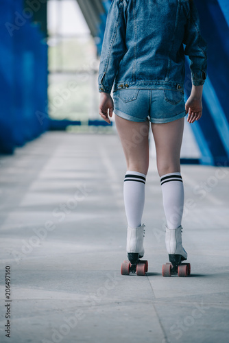 back view of fashionable woman in denim clothing and high socks roller skating alone