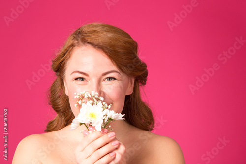 Close up female portrait. Beautiful adult woman with flowers on a pink background. Red hair woman.