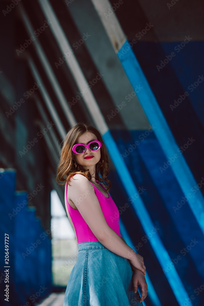 Fototapeta premium portrait of stylish smiling woman in pink retro sunglasses and denim skirt