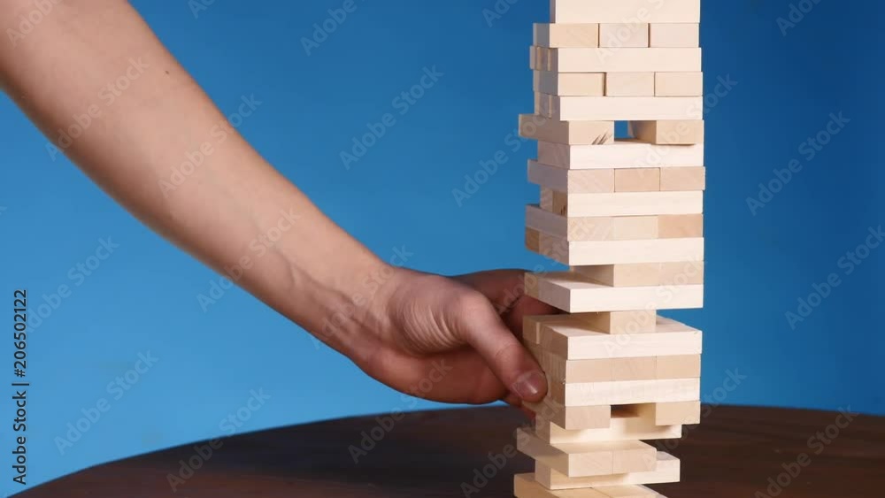 hands of Young man plays jenga on blue background, close-up. A man builds a tower of blocks while playing jenga hands of Young man plays jenga on blue background, close-up. A man builds a tower of blocks while playing jenga