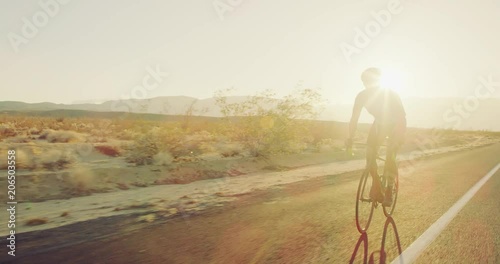 Slow motion young man cycling on road bike outside on desert road at sunset with lens flare 