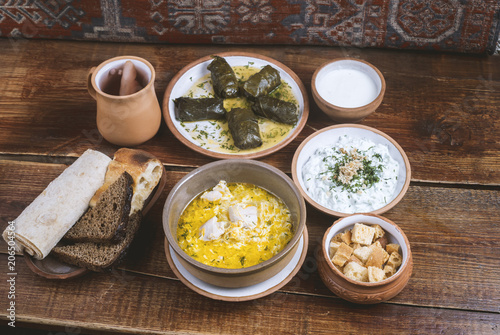 Middle Eastern cuisine dishes in ceramic plates on a wooden table. Chicken soup, dolma with grape leaves, tzatziki, Greek yogurt, rusks, bread, lavash, and compote. photo