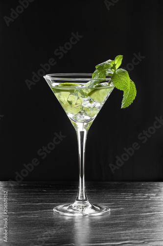 Fresh summer cocktail with green lime slices, crushed ice and mint leaves in a martini glass backlit on black background