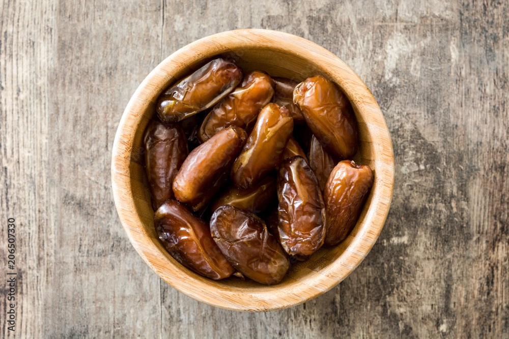 Dates food in wooden bowl on wooden table. Top view Dates food in wooden bowl on wooden table. Top view