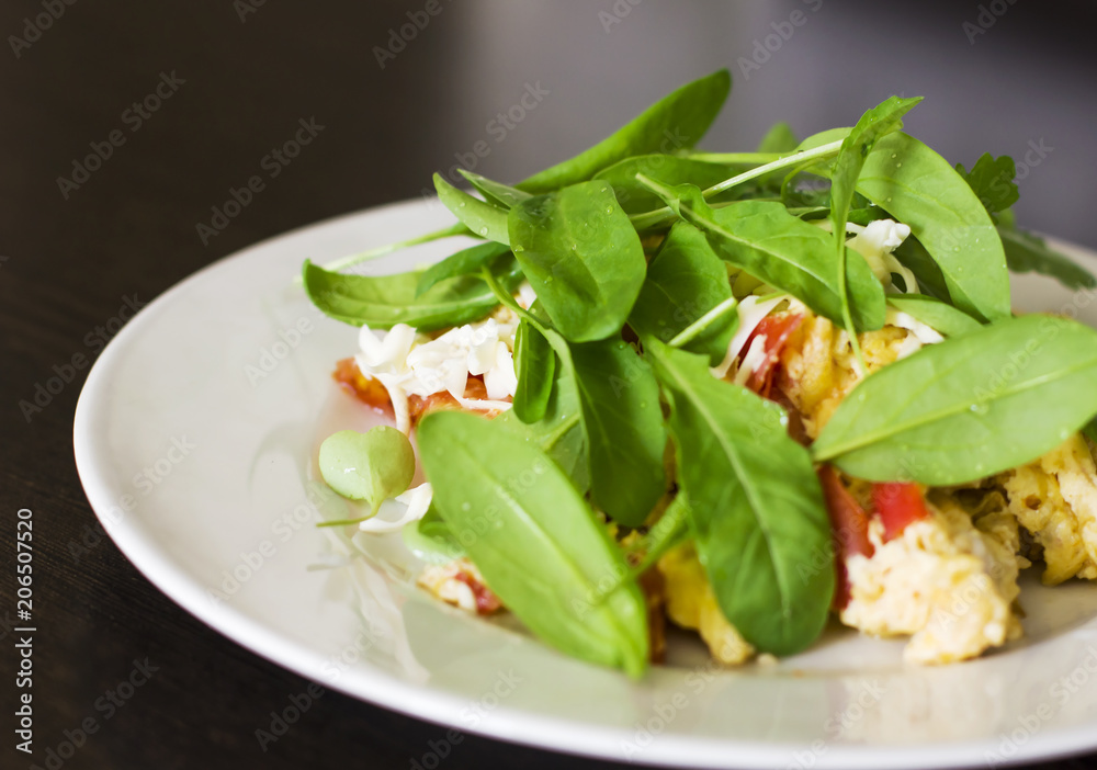 Egg omelet with tomato and fresh arugula spinach in white plate on wooden background Egg omelet with tomato and fresh arugula spinach in white plate on wooden background