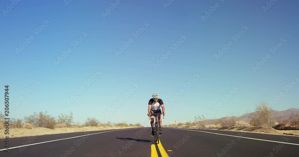 Young healthy man cycling on road bike outside on desert road on sunny day with blue sky in background Young healthy man cycling on road bike outside on desert road on sunny day with blue sky in background