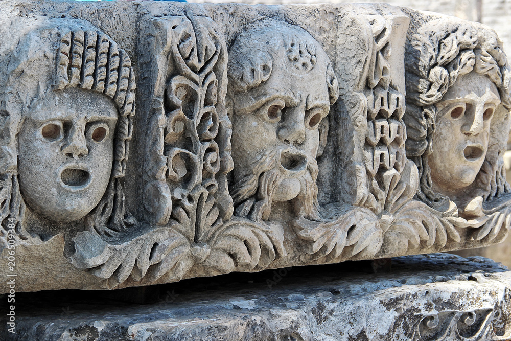 Theatrical masks adorn the stone blocks in front of the facade of the theater. The ancient Greco-Roman theatre in Myra (Demre — Turkey) Theatrical masks adorn the stone blocks in front of the facade of the theater. The ancient Greco-Roman theatre in Myra (Demre — Turkey)
