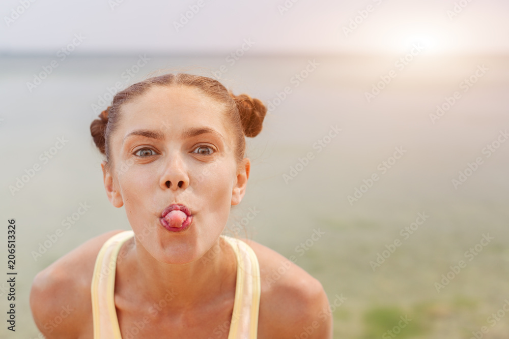Portrait of young stylish laughing girl model summer natural makeup outside on the beach. Looking at camera showing her tongue