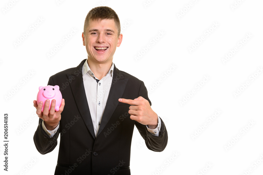 Studio shot of young happy businessman smiling while holding pig Studio shot of young happy businessman smiling while holding pig