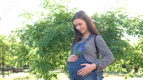 A young, beautiful, pregnant girl, near a tree, dressed in overalls.
