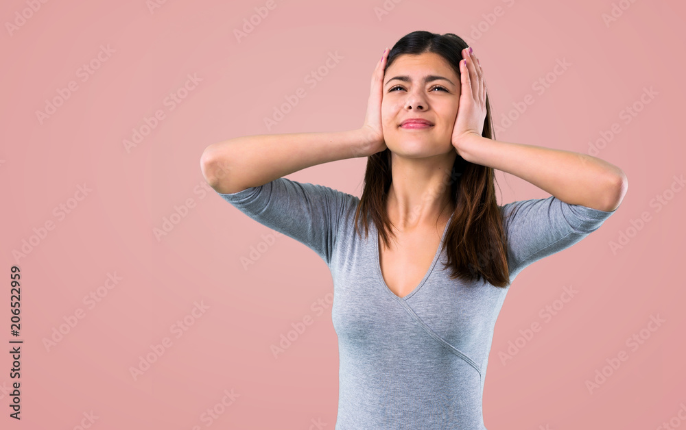 Teenager girl covering both ears with hands on pink background Teenager girl covering both ears with hands on pink background